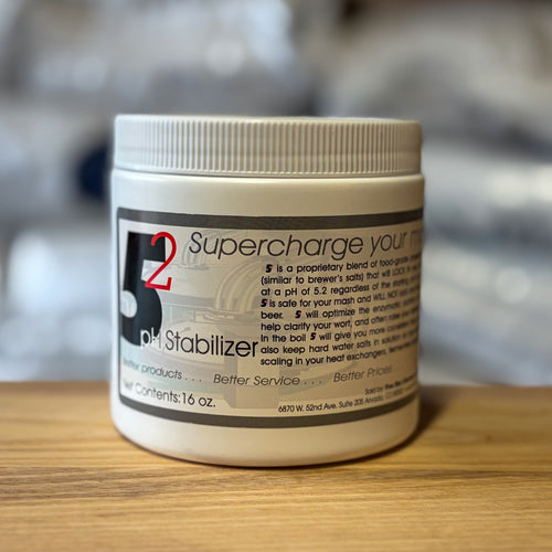 A white plastic jar of 5.2 pH Stabilizer brewing mash chemistry adjuster, resting on a wooden surface with a blurred gray background.