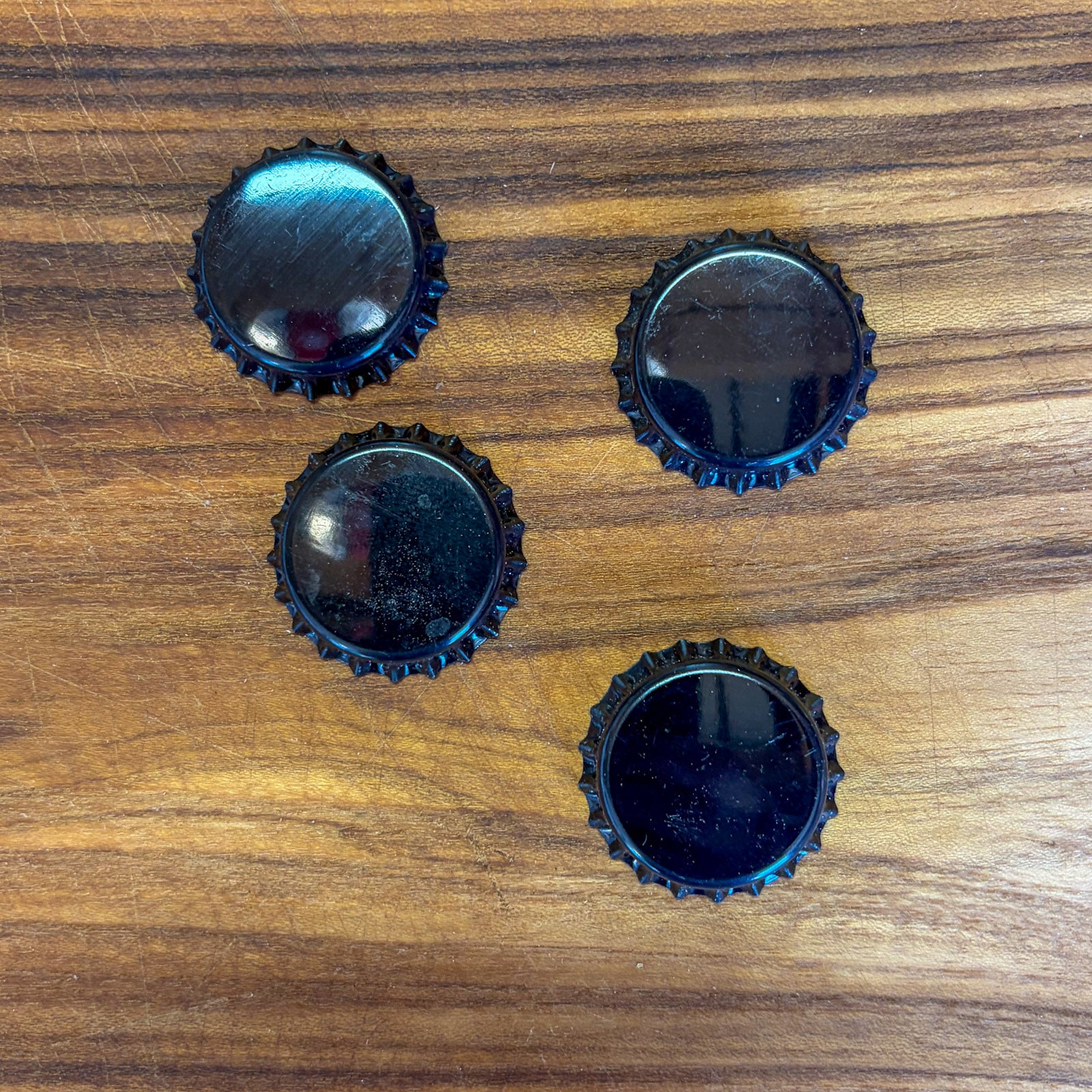 Four black bottle cap charms with a glossy finish, arranged on a brown wooden surface.