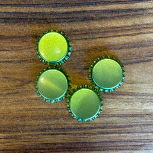 Four gold bottle cap charms with a metallic finish, arranged on a dark wood grain surface.
