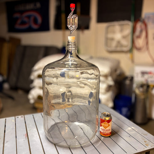 A glass carboy on a metal table with carboy stopper #7 and an s airlock installed