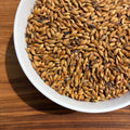 A bowl of dingemans special b crystal malt in the sun showing 120 lovibond color with a wood background