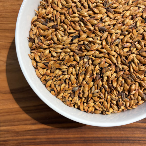 A bowl of dingemans special b crystal malt in the sun showing 120 lovibond color with a wood background