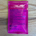 A single pink fermentis SafAle T-58 dry brewing yeast packet by Fermentis lies flat on a light wood surface. The front of the packet is printed with product details in white and light blue text.