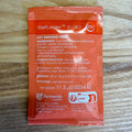 A single orange packet of Saflegen E-30 Dry Brewing Yeast by Fermentis lesaffre, placed flat on a light-colored wooden surface. The packet contains product details in white text and features a white and red logo.