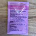 A single pink and white Fermentis SafLager W-34/70 dry lager yeast sachet lying flat on a light brown wooden surface. The front of the packet displays the product name, ingredients, characteristics, dosage, pitching instructions, and Fermentis branding.