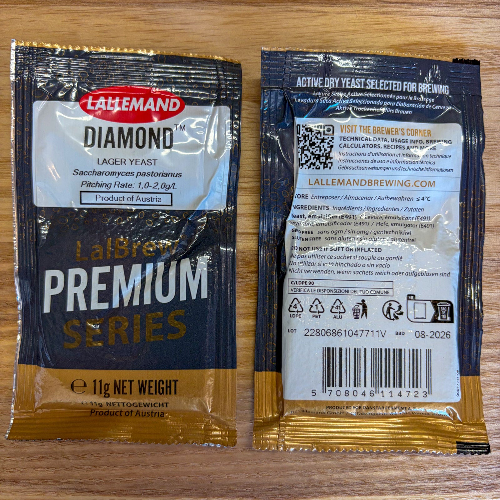 Two Lallemand Diamond Lager Yeast packets shown front and back on a light wood surface. The front packet is black with gold and white text, and the back packet shows brewing information, QR code, ingredients, and barcode.