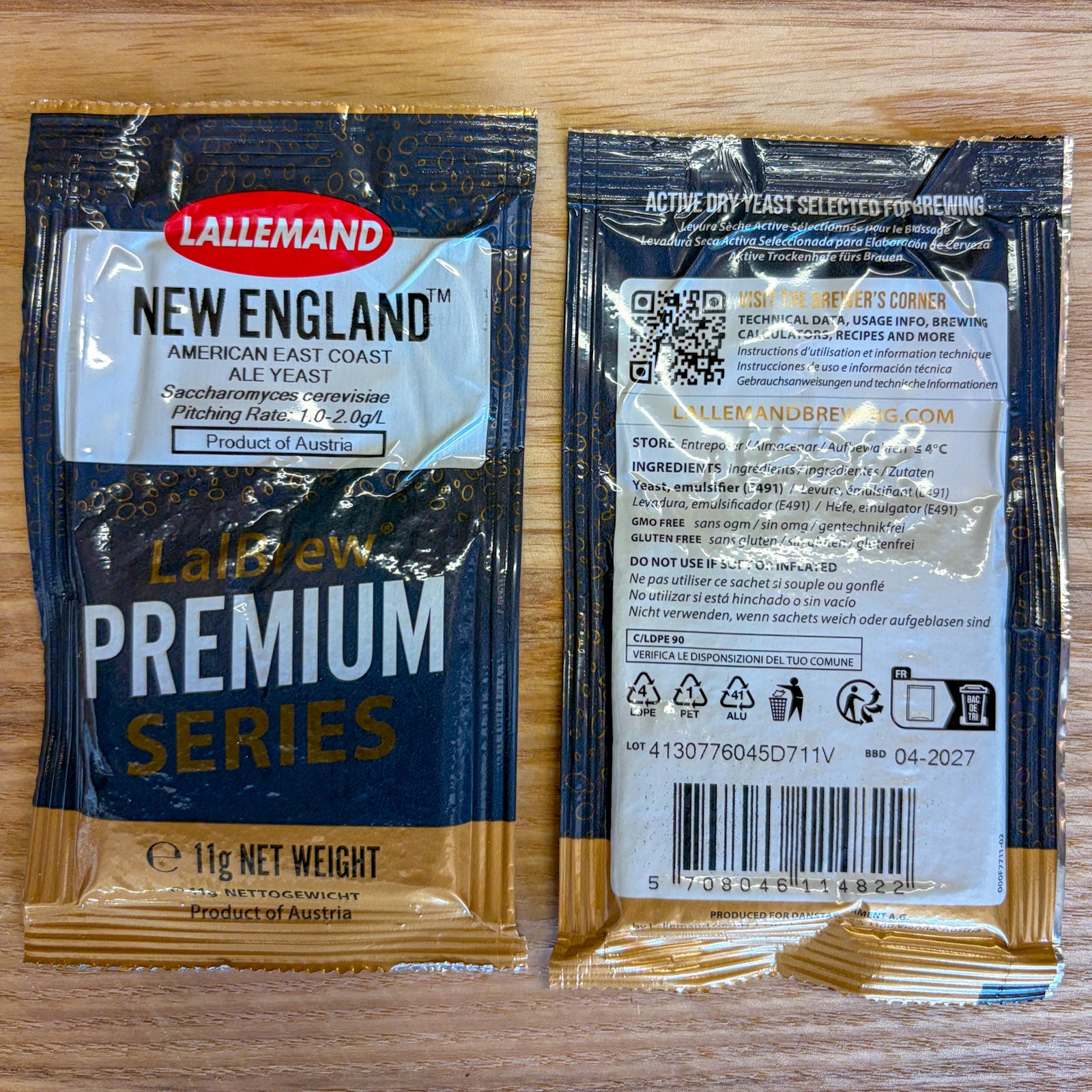 Two 11g packets of Lallemand New England Premium Series Ale Yeast shown side-by-side on a light wood background, displaying both the front and back packaging details.