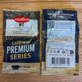 Two LalBrew Premium Series wit ale yeast packets shown on a wooden surface, with the front and back packaging visible. The packets are dark blue and gold with white text and a red LalBrew logo.