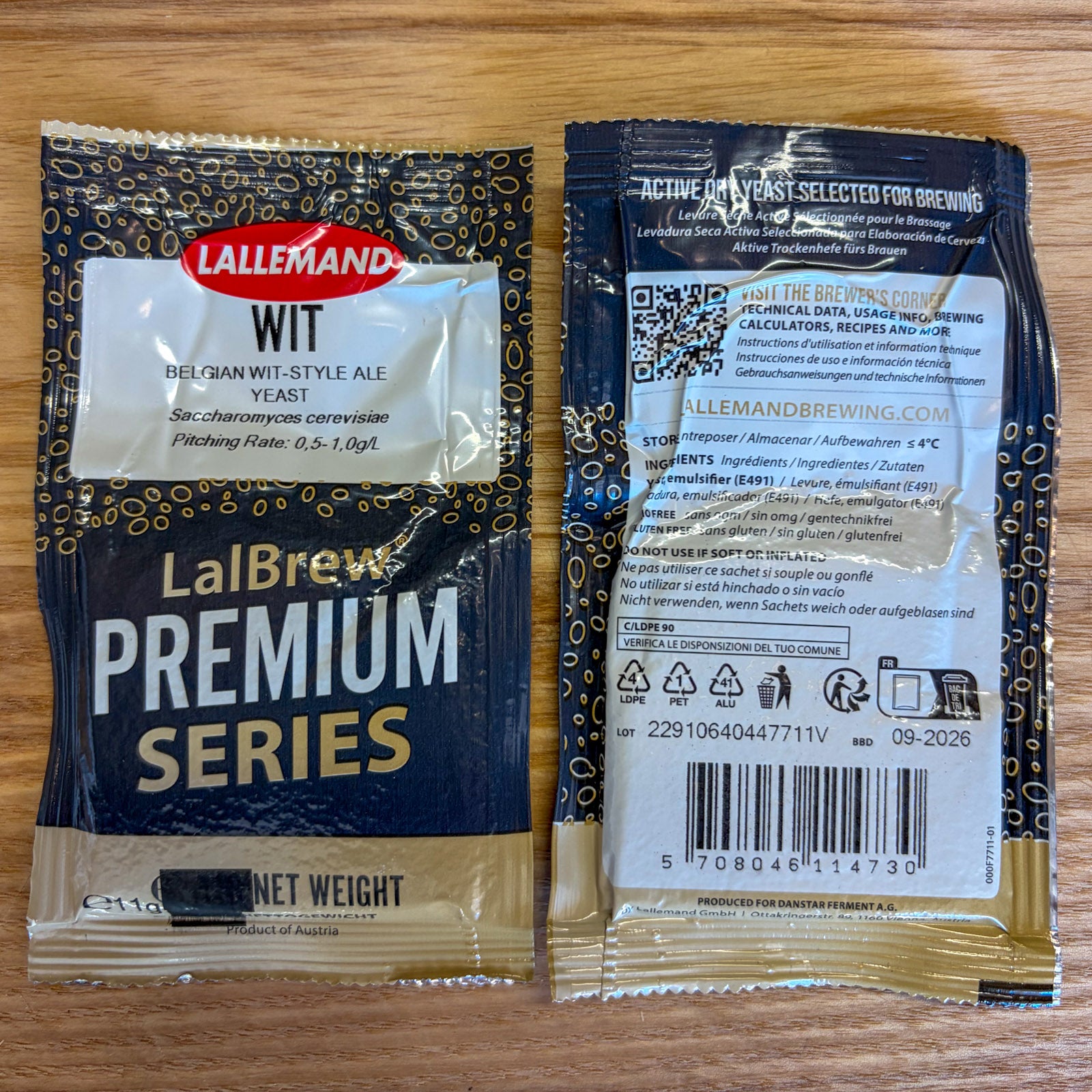 Two LalBrew Premium Series wit ale yeast packets shown on a wooden surface, with the front and back packaging visible. The packets are dark blue and gold with white text and a red LalBrew logo.