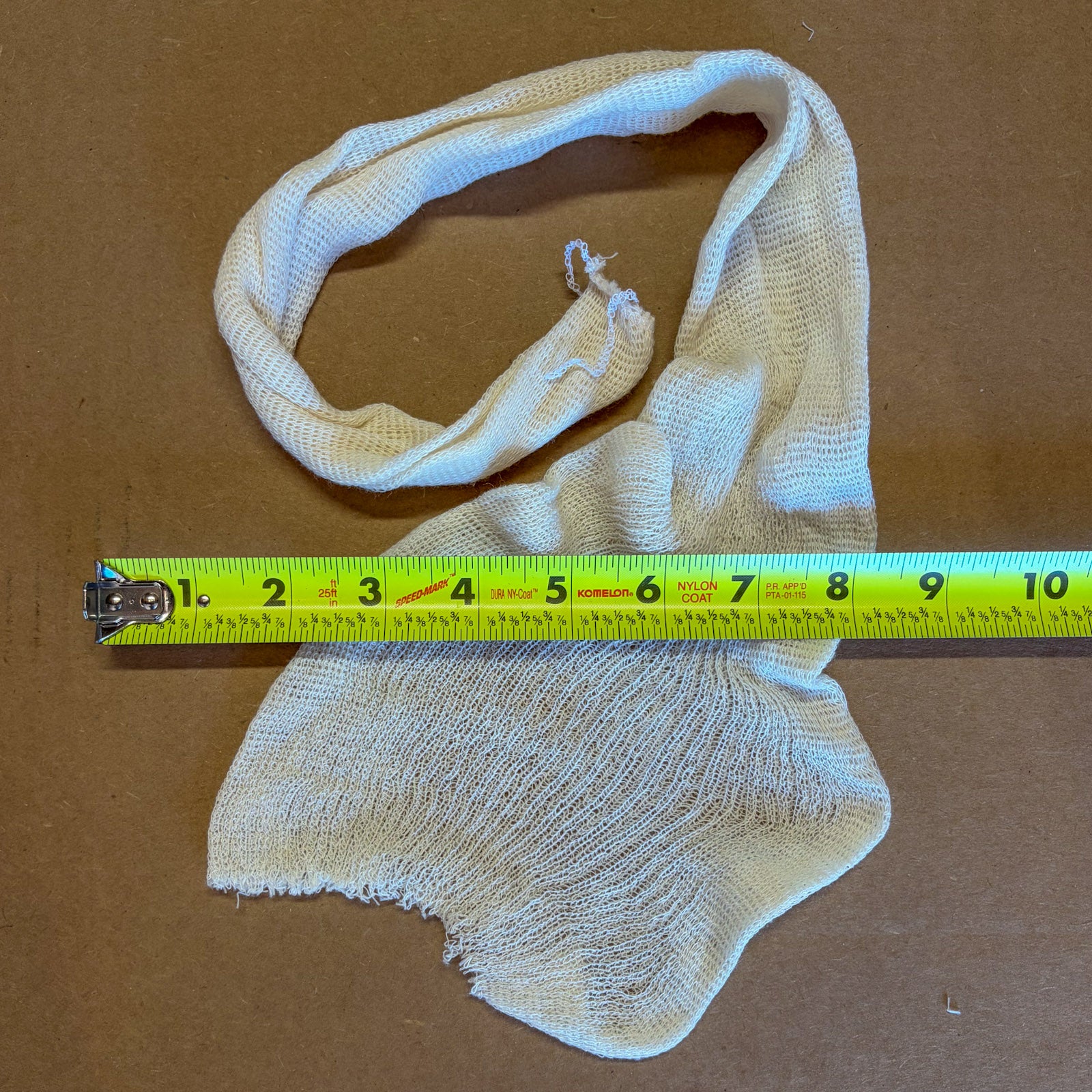 A large muslin bag for homebrewing measuring 1’x3’ on a cardboard surface