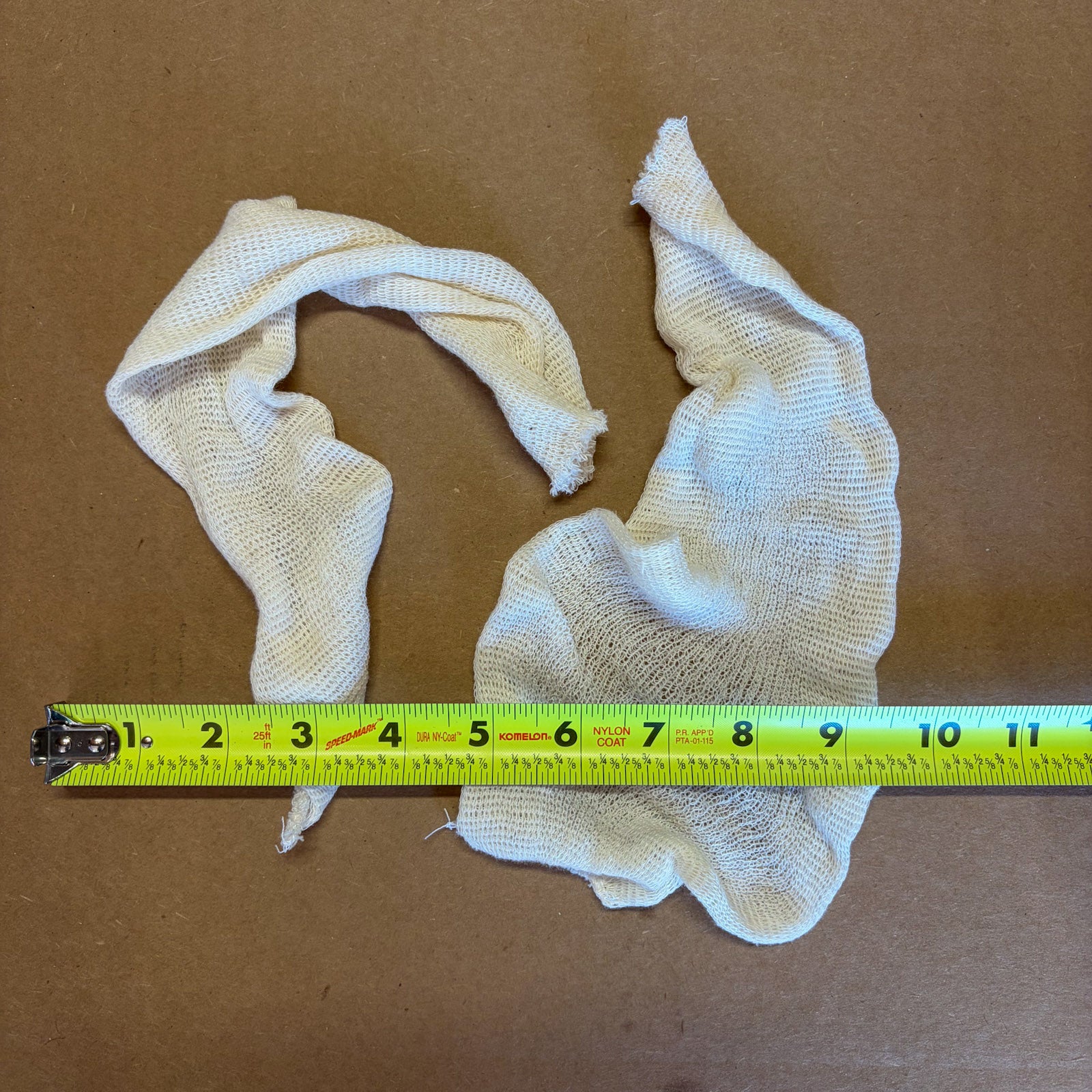 A pair of off-white small muslin bags measuring 5”x15”, displayed on a brown background with a yellow tape measure underneath for scale.