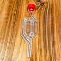 A clear plastic S double bubble fermentation airlock with a red cap, placed on a wooden surface.