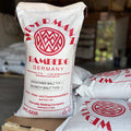 A pallet of weyermann Munich type 1 malted barley, with one bag standing up showing the label, in a garage setting