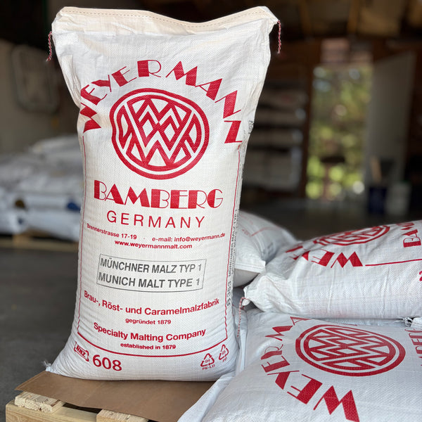 A pallet of weyermann Munich type 1 malted barley, with one bag standing up showing the label, in a garage setting