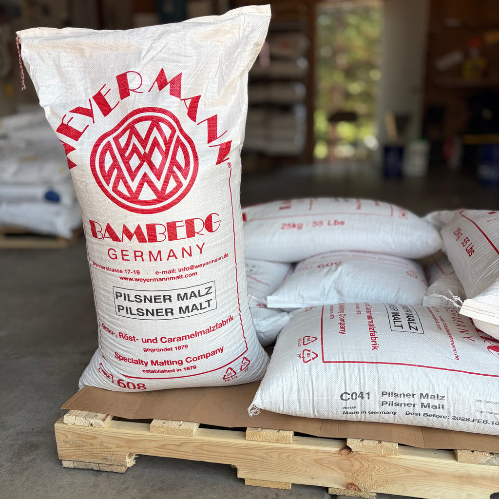 Sacks of weyermann pilsner malted barley on a pallet, one standing up showing the label and others lying down.