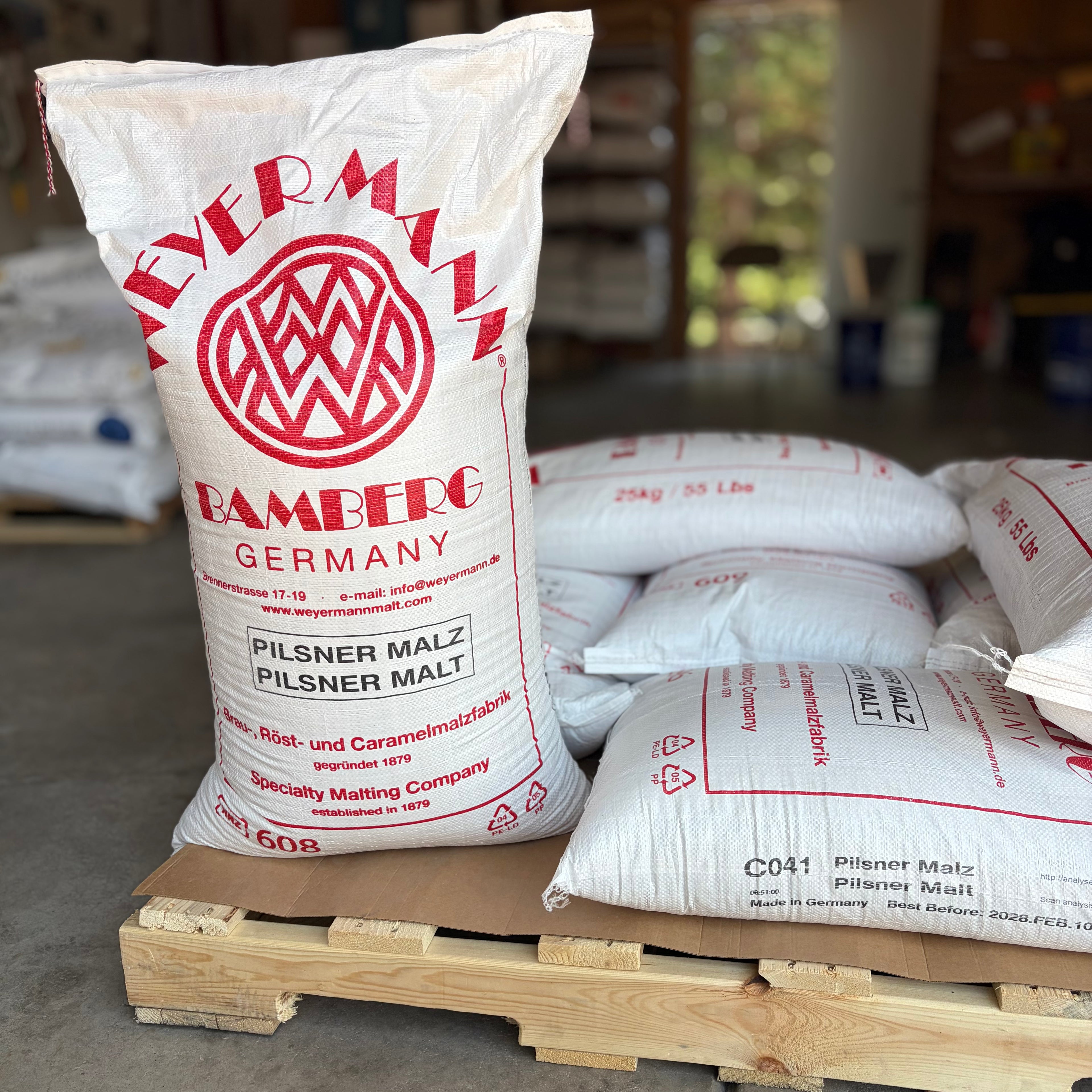 Sacks of weyermann pilsner malted barley on a pallet, one standing up showing the label and others lying down.