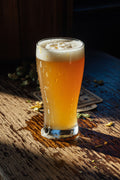 moody low light shot of a pint of hazy pale ale on a wood table with centennial hops