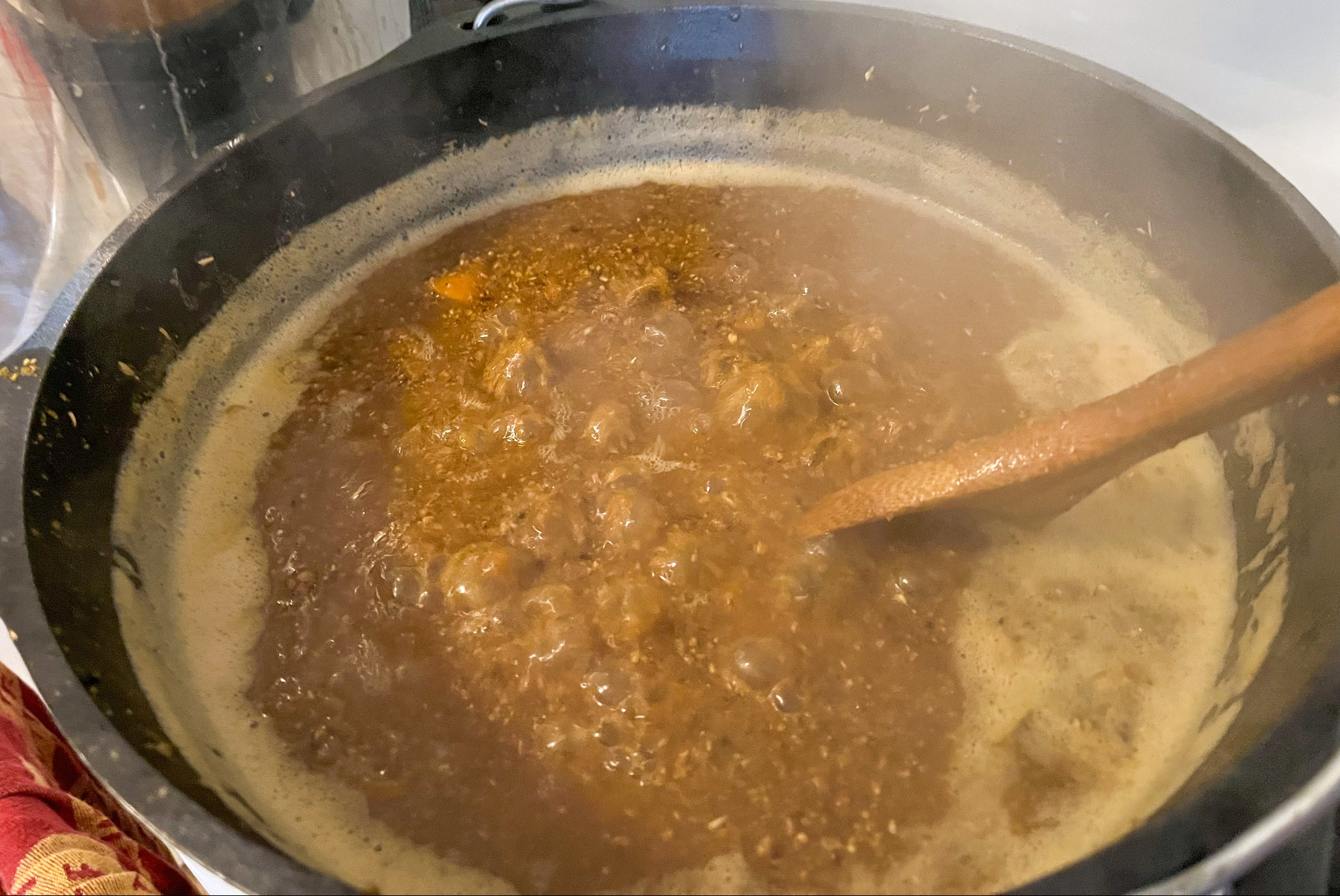 a close up of a homebrew decoction mash with boiling wort in a cast iron dutch oven and a wooden spoon